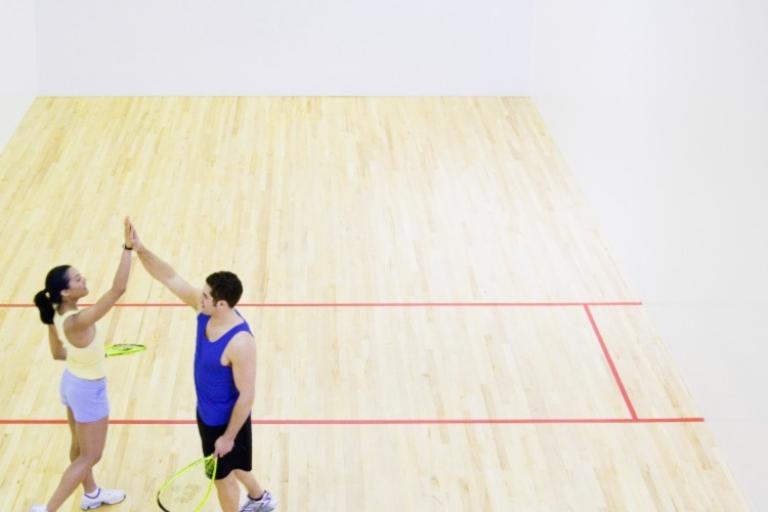 Man and woman doing a high five in the middle of an empty Squash court. 