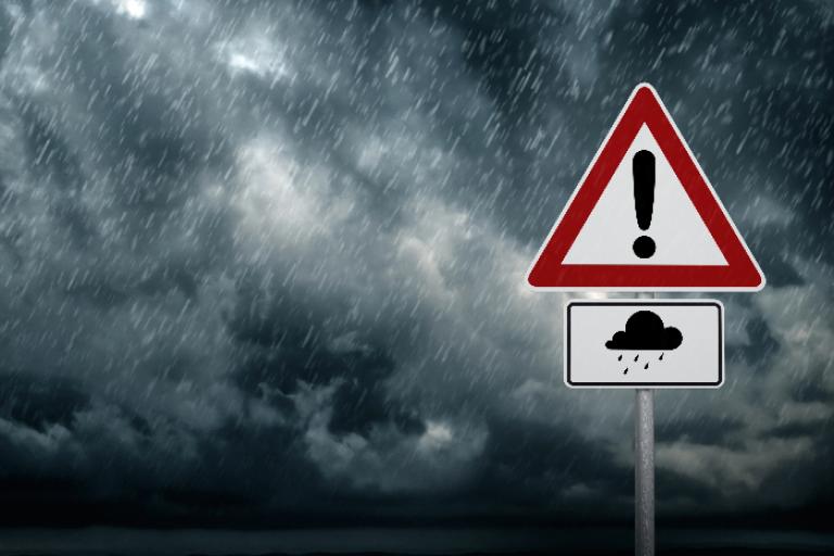 Rain clouds with heavy rain falling. A warning road sign with a rain cloud sign. 