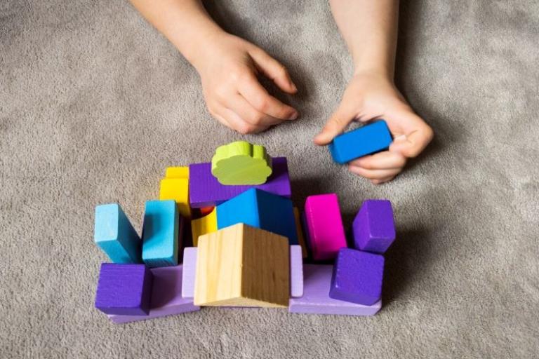 Pair of hands using building blocks of different shapes and colours to build a home