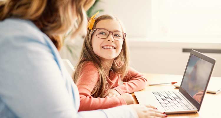 Child with glasses smiling at an adult with laptop on table