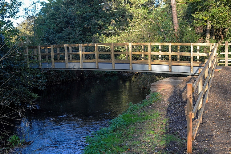 New Shepherd meadows footbridge with river running underneath and trees behind it.