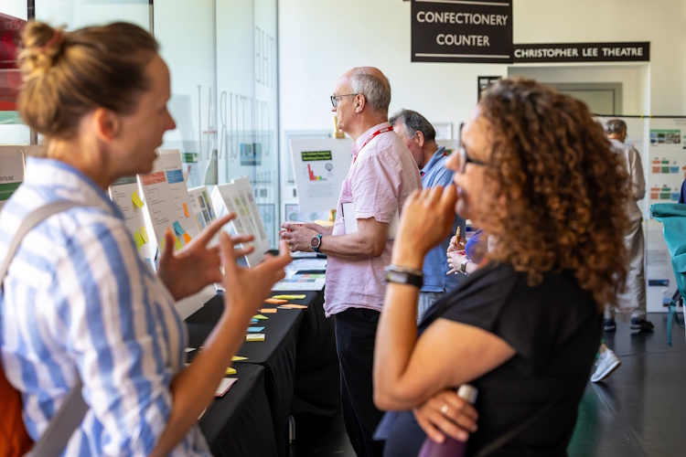 In the foreground, two women are in deep conversation. Behind them a man examines a stall at the Bracknell Forest climate change summit.