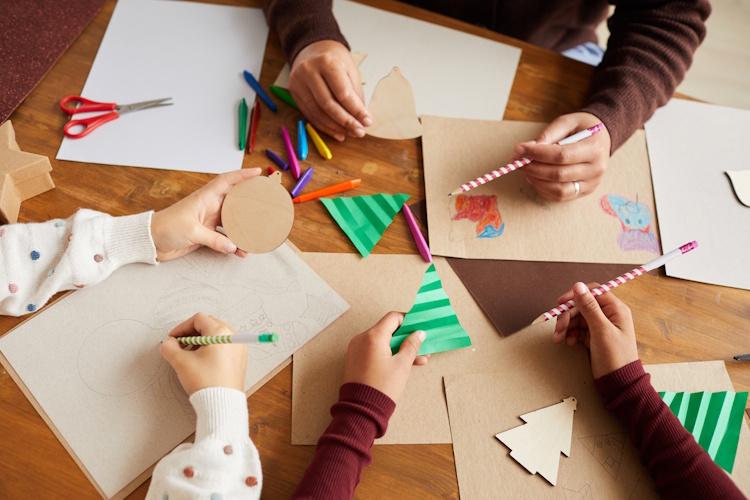 The hands of several children sat around a table making Christmassy crafts.