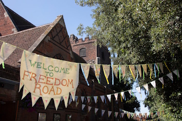 Bunting and a banner in neutral colours hung outside the Colchester Arts Centre. The banner in the middle reads "Welcome to Freedom Road".