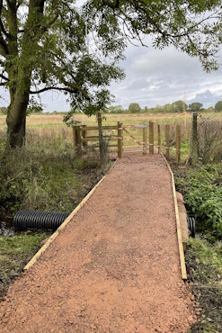 The southern entryway for Frost Folly. There is a wide, gravelled path which leads to a wooden gate.