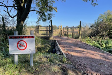 Frost Folly's southern entranceway. Beside a wide, gravel path is a sign that says "strictly no parking".