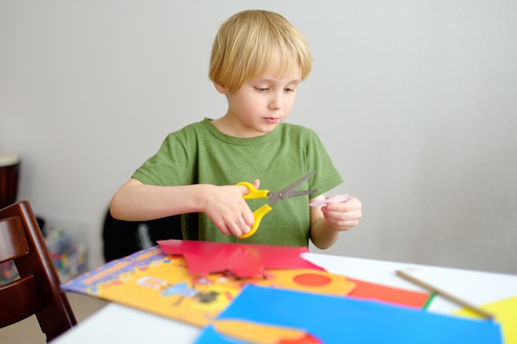 A boy carefully cuts out a circle of paper.
