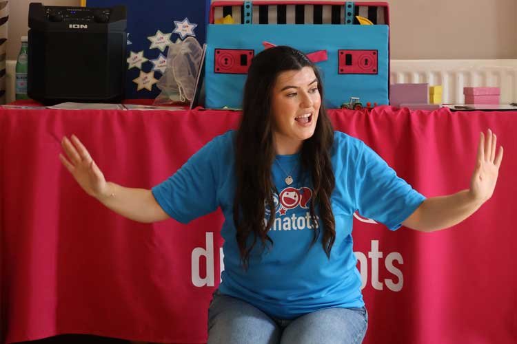 Woman wearing a blue drama tots tshirt with hands outstretched