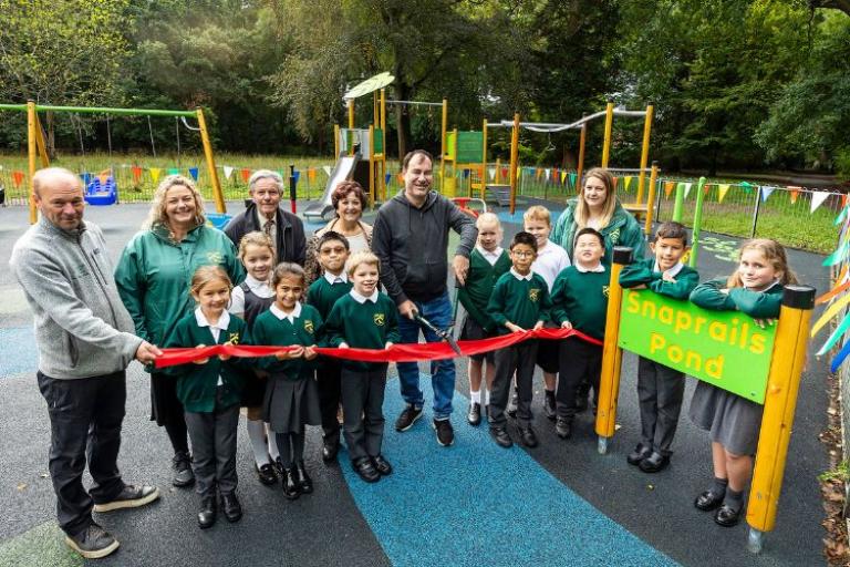 Children and adults standing in a playground whilst getting ready to cut the unveiling ribbon