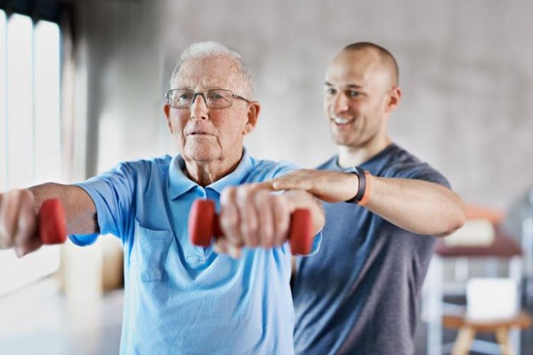 Carer helps older gentleman lift weights