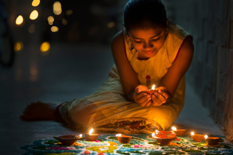 A young girl holding a candle in her hands with several other colourful candles on the floor in front of her.