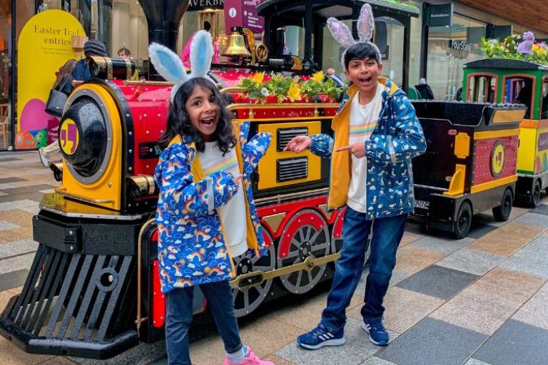 Photo of the Easter Express train at The Lexicon in Bracknell. Two children standing in front smiling and pointing at the train.