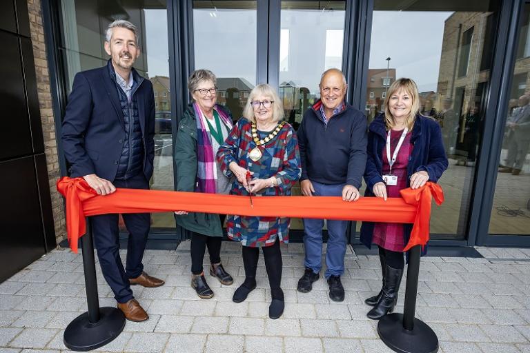 five people behind a red ribbon for a ribbon cutting ceremony