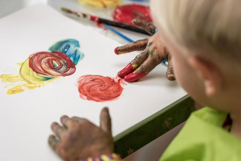 blonde toddler with green apron finger painting