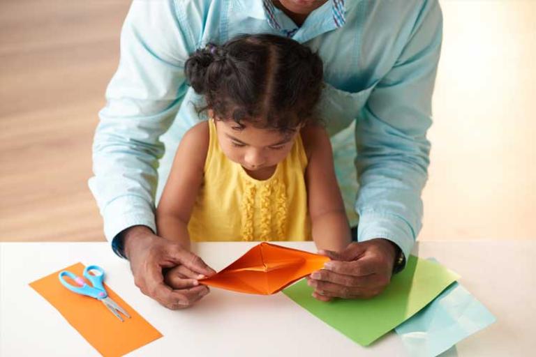 Little girl making colourful boat crafts with the help of her carer