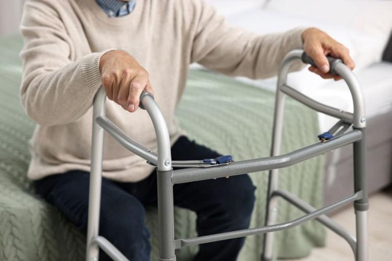 an elderly man sitting on a bed holding a walking frame