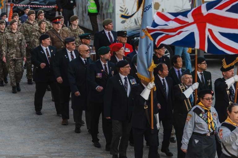 Parade of uniformed adults and teenagers, including holding up a large union jack flag