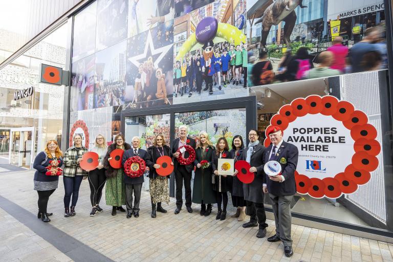 Line of people outside a shop with poppies in the window - the people are all holding poppy merchandise.  