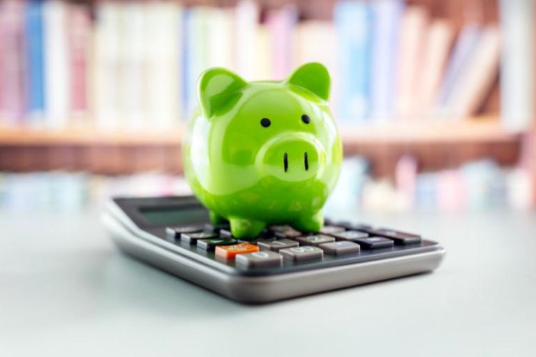 A green piggy bank sitting on a calculator 