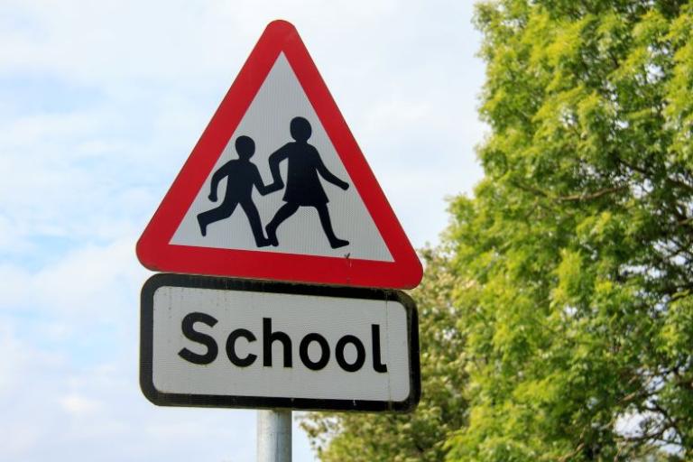 a red triangle road sign with image of two children and the word school below