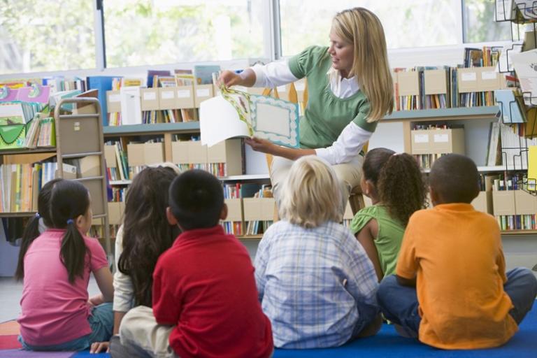 A person reads a picture book to a group of children sitting on the floor in a library