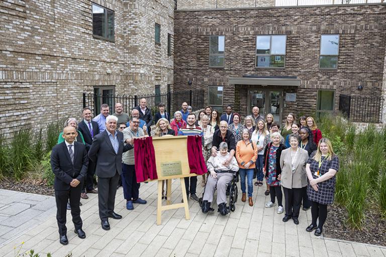 Group of people outside by a plaque celebrating the opening of a new building.building. 