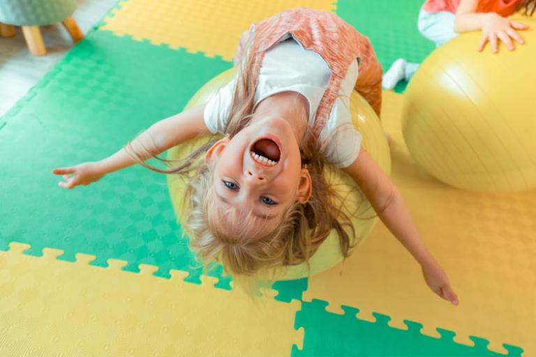 Smiling girl lying backwards on a large yellow ball