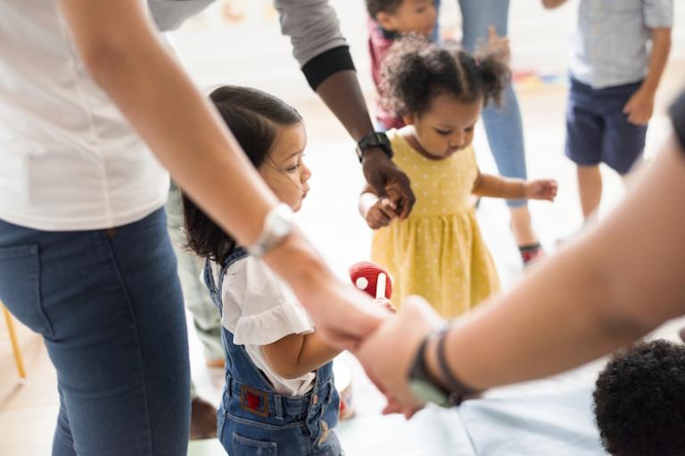 Toddlers and parents stand holding hands in a circle.
