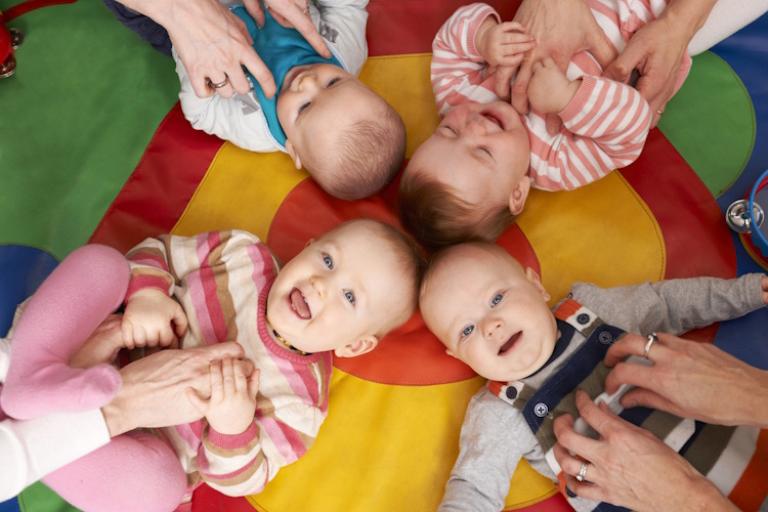 Four babies lie on their backs being tickled.