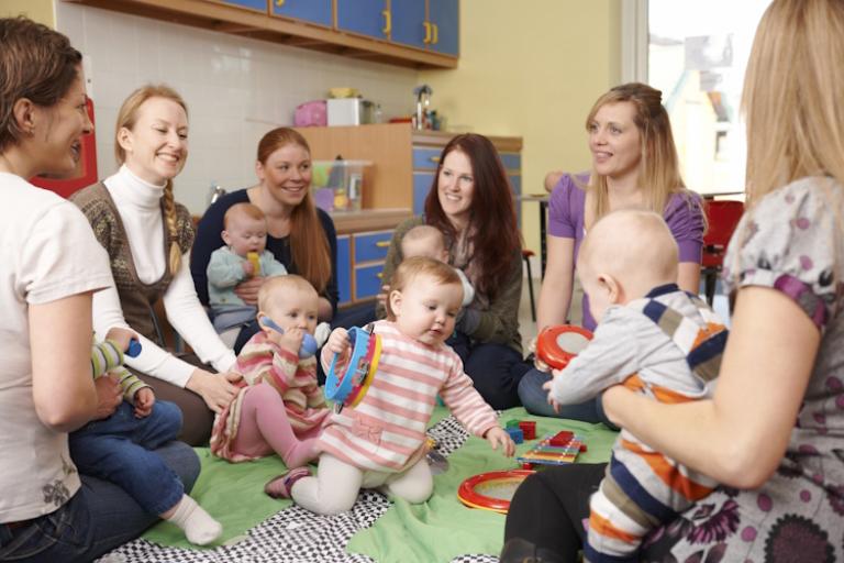 A group of mothers and babies sit in a circle playing.