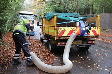 Man using large hose to suck up leaves on the pavement