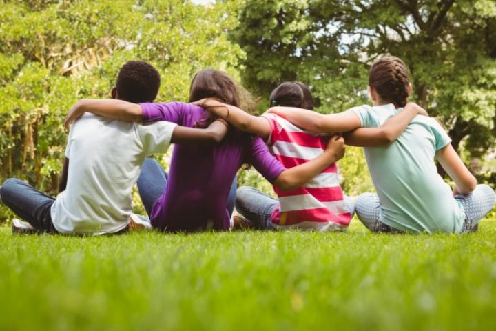 four children sitting on the grass, arms round each other