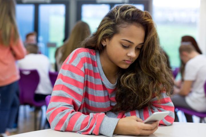 Teenage girl sitting at table, looking on mobile