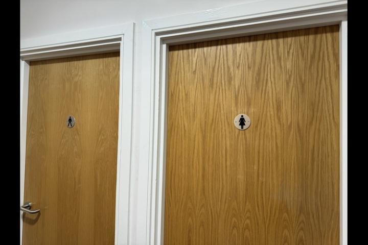 Two oak doors - one has a female symbol in the middle and the other has a male symbol