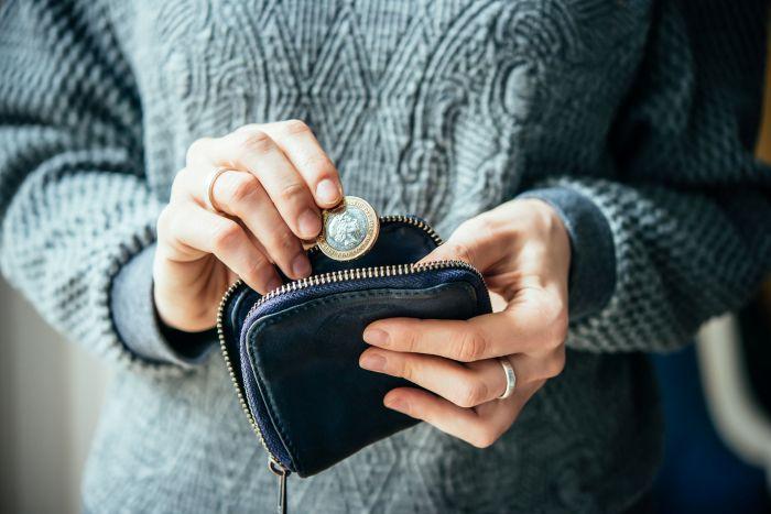 a person holding a coin over an empty purse