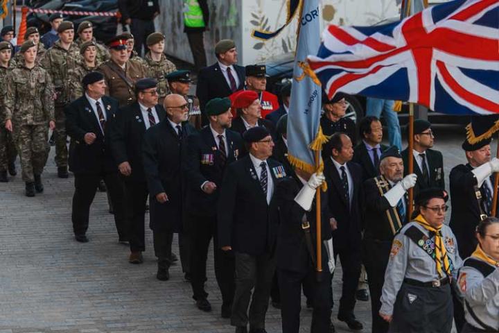 Parade of uniformed adults and teenagers, including holding up a large union jack flag