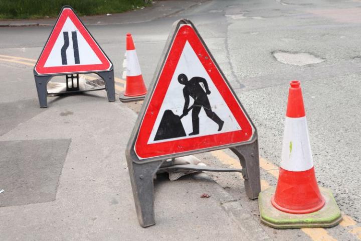 two roadwork signs and two traffic cones on the roadside