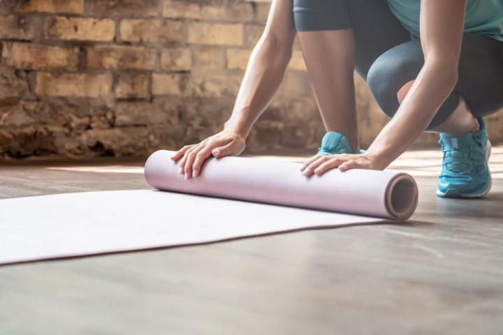 A person bends down to unroll a yoga mat.