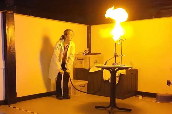 Person in white overalls doing a science experiment with a big burst of flame