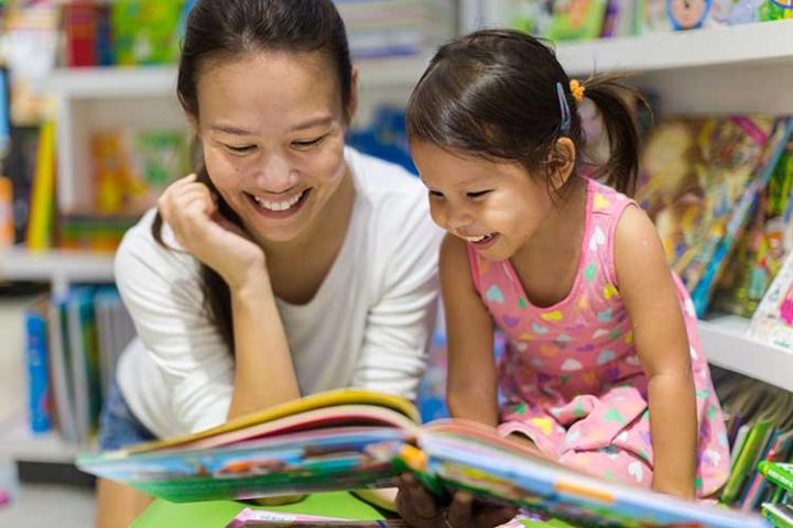 Mother and young daughter reading in library