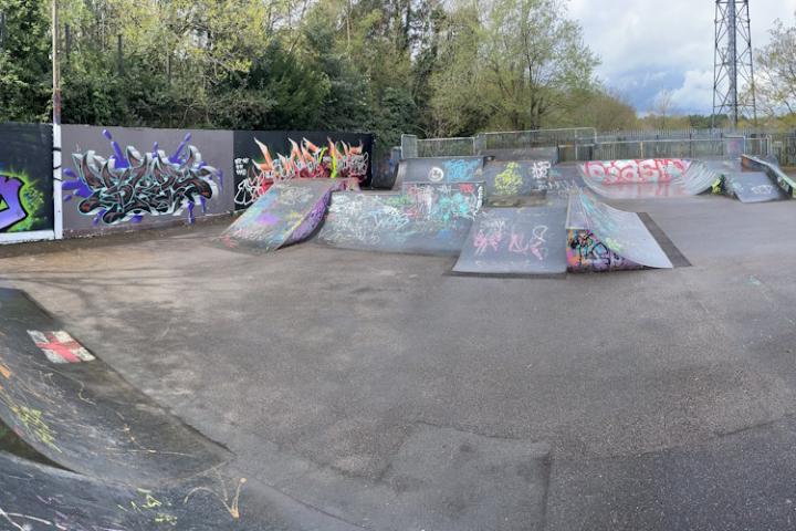 A large skatepark with several ramps in the centre and colourful graffiti displays around it.