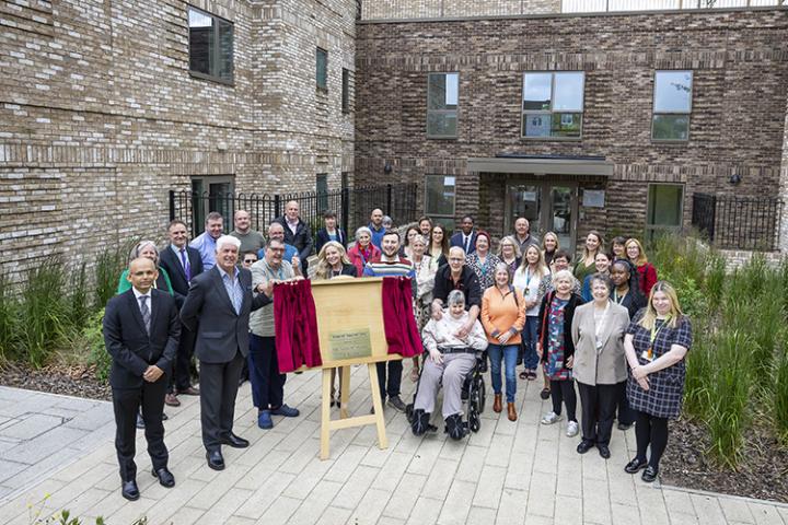 Group of people outside by a plaque celebrating the opening of a new building.building. 