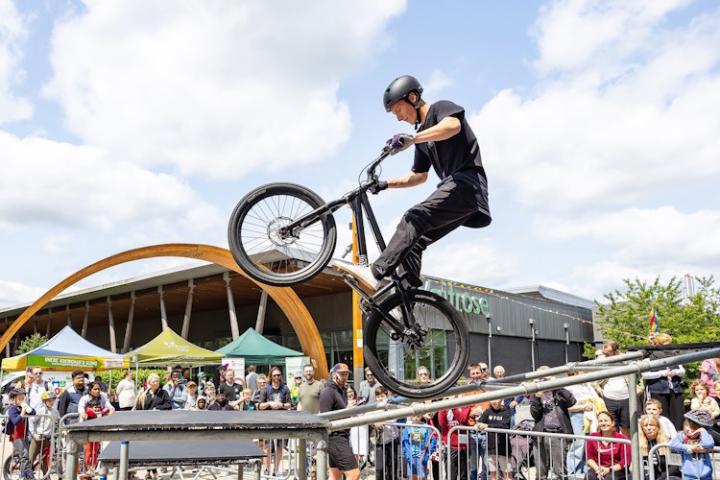 A man on a stunt bike does a wheely down a thin ramp in front of a crowd of people.