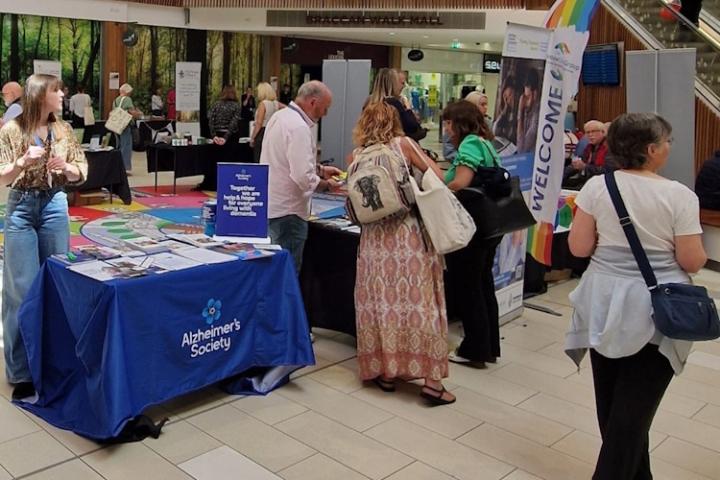 Lots of people gather around stalls in Princess Square shopping centre. The nearest stall is for the Alzheimer's society.