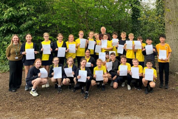 a group of school children holding sheets of paper in a woodland setting