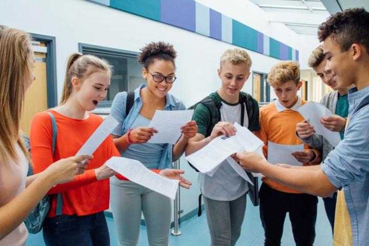 a group of teens looking at exam results on sheets of paper