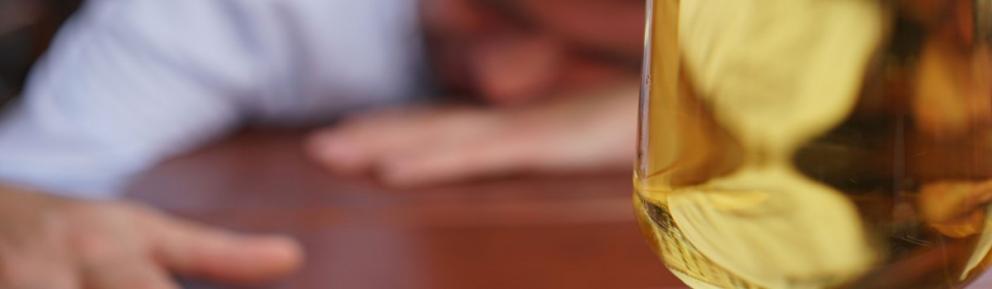 Glass on a table with person with head on their hands in blurry background