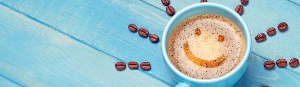 blue coffee cup with smiley face in the foam and coffee beans outside the cup like rays of sun