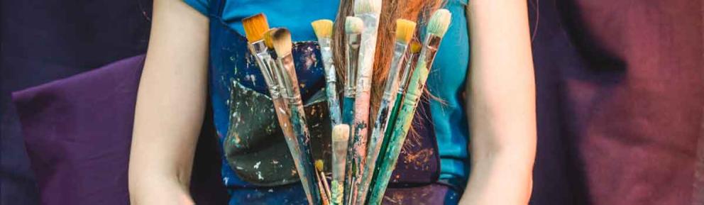 Person wearing apron holding pot of paintbrushes