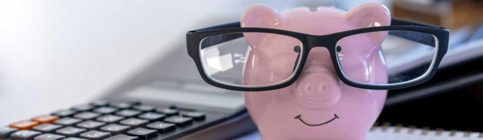 Pink smiling piggy bank with glasses on and calculator beside it